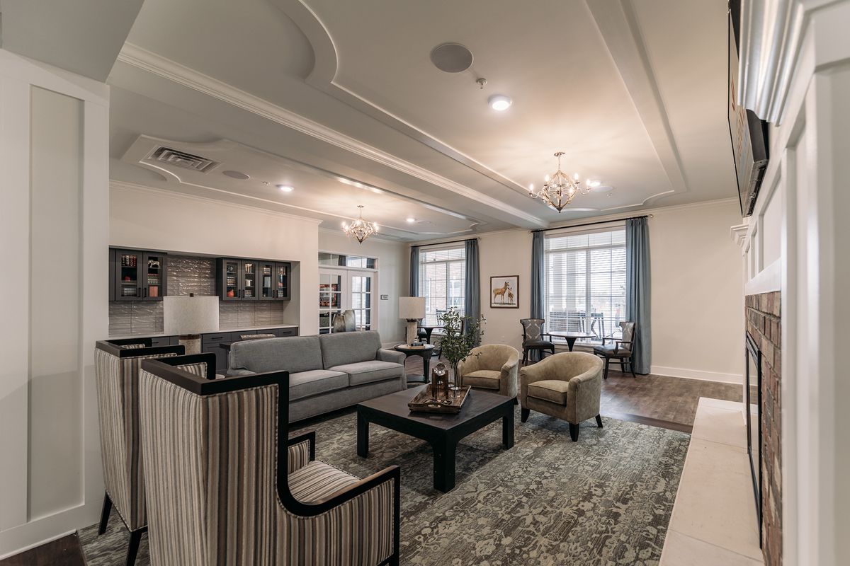 A spacious and elegantly decorated living room featuring a comfortable seating area with a sofa, armchairs, and a coffee table under two chandeliers.