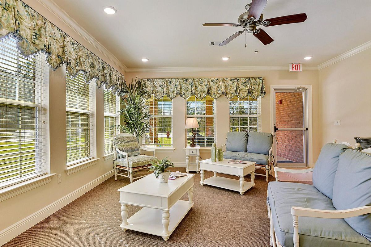 A bright living room with comfortable seating, a ceiling fan, and large windows.