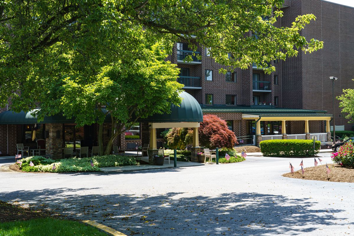 A building entrance surrounded by lush greenery and a shaded driveway.