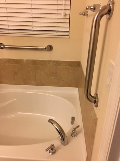 A bathroom with a bathtub featuring safety grab bars on the wall.