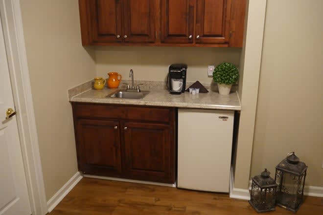 A compact kitchen area with wooden cabinets, a small sink, mini-fridge, and countertop appliances.