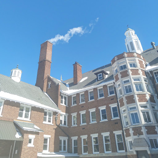 A close-up view of an architectural structure featuring brickwork and a chimney with smoke against a clear blue sky.