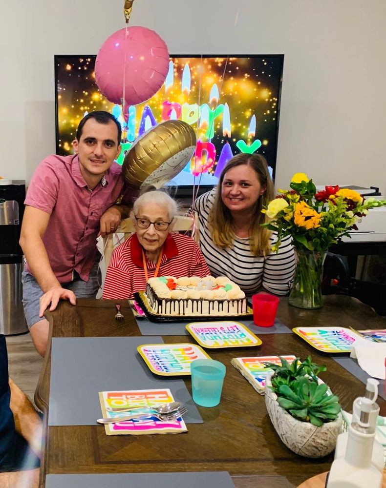 A joyful family celebration with an elderly woman surrounded by loved ones, a birthday cake, and festive decorations.