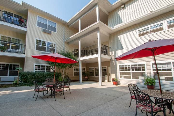 A sunny courtyard in an apartment complex with outdoor tables and red umbrellas.
