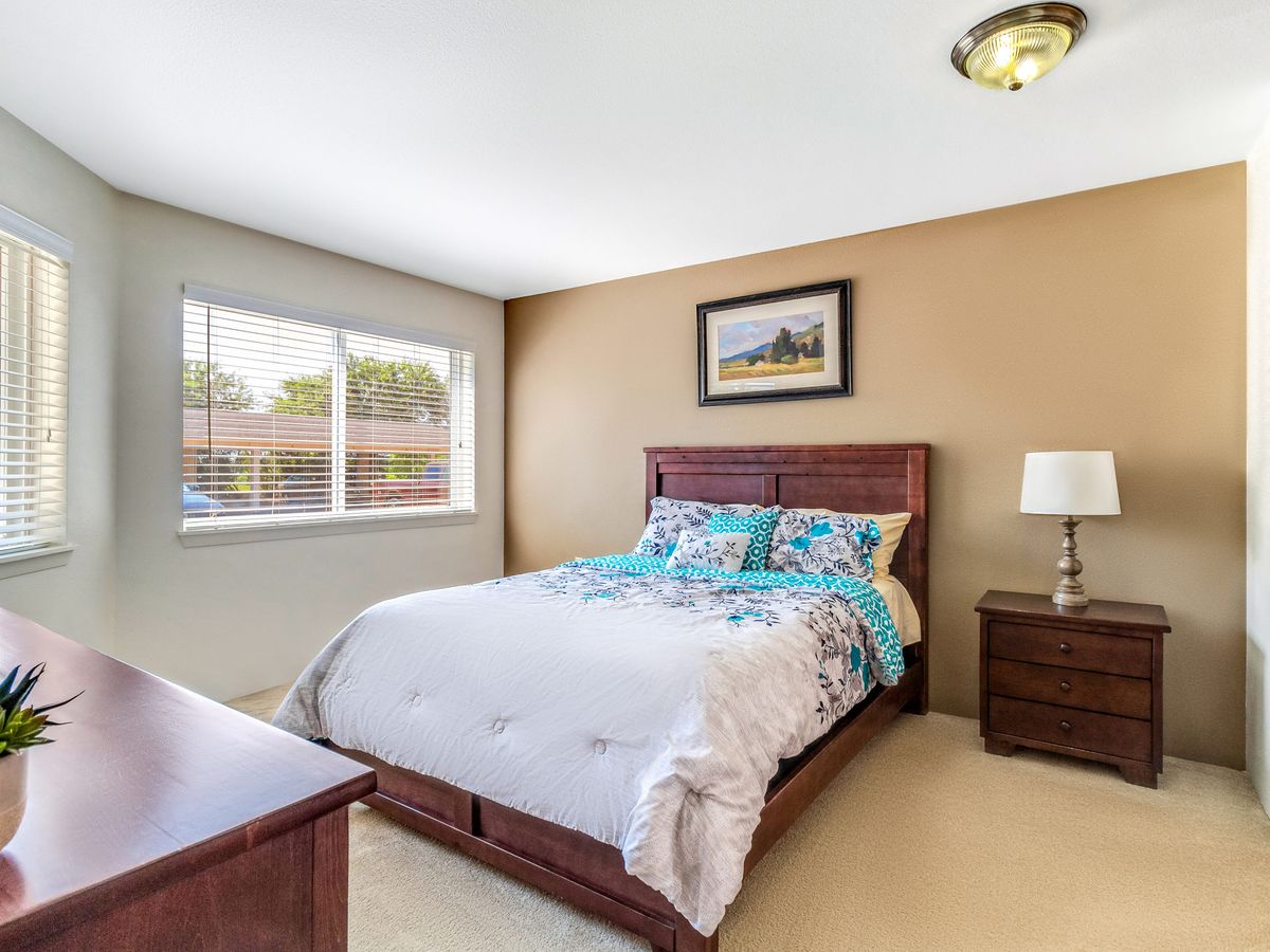 A cozy bedroom with a large bed, bedside table with a lamp, and a window allowing natural light.