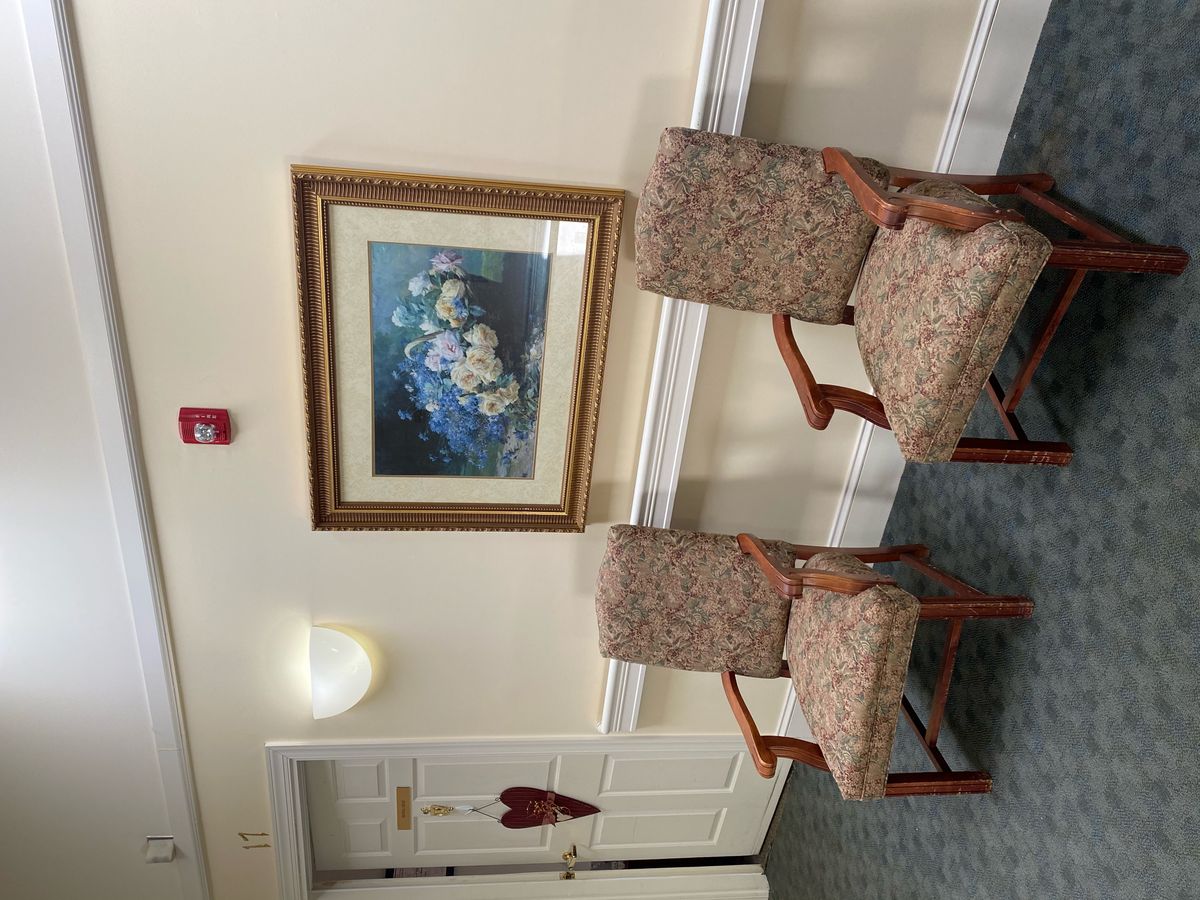 A cozy waiting area with two chairs and a floral painting on the wall.