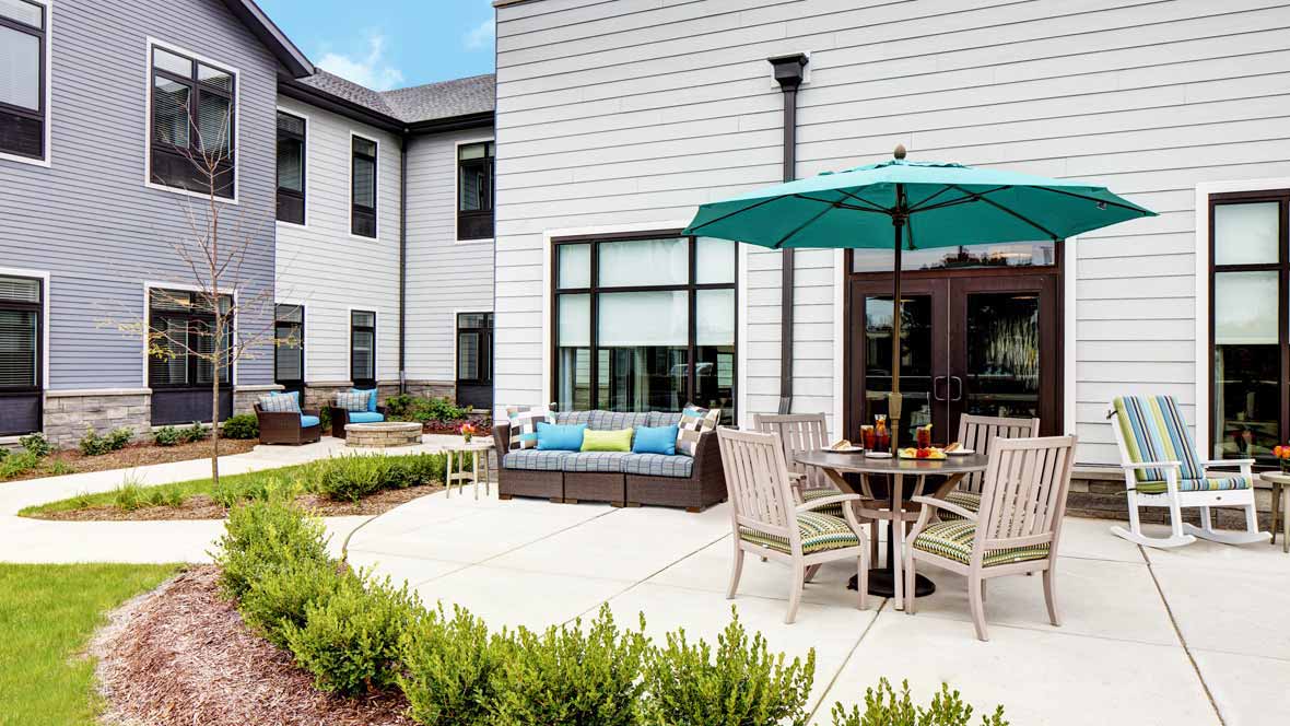 A modern patio with outdoor seating and an umbrella, surrounded by a well-maintained garden.