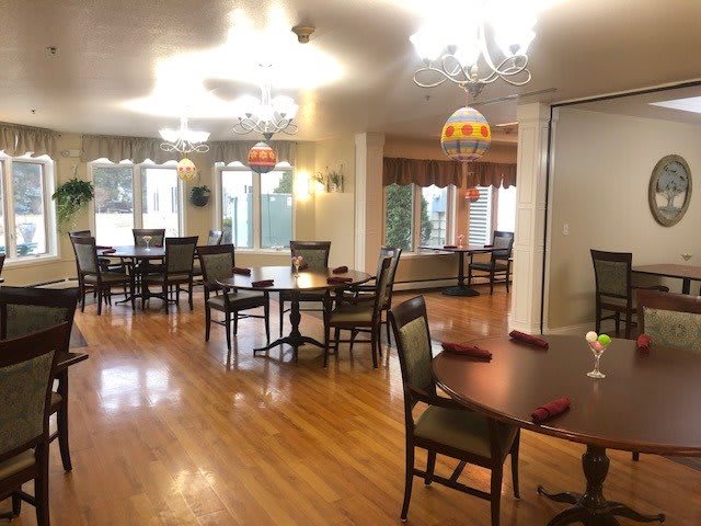 A well-lit dining room with several tables and chairs on a wooden floor.