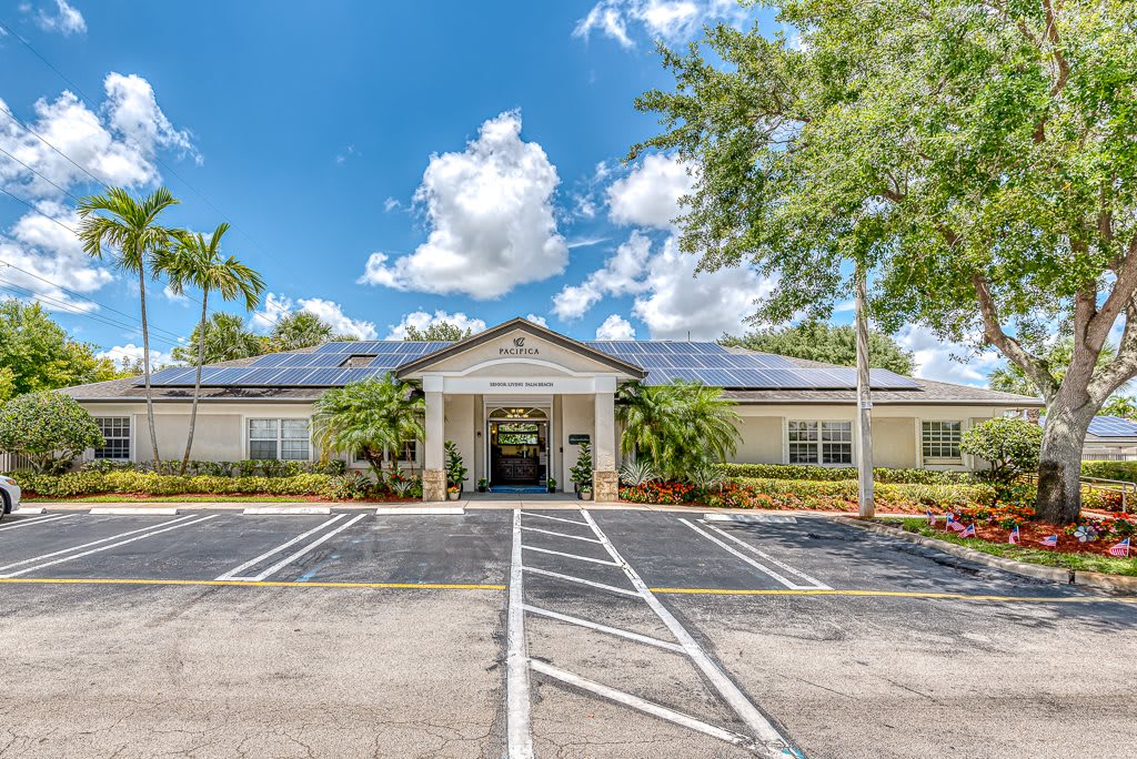 A one-story building with a prominent entrance, surrounded by trees and a parking lot, under a partly cloudy sky.