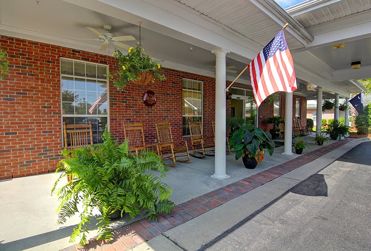 A charming front porch with rocking chairs, lush plants, and an American flag adorning a brick house.