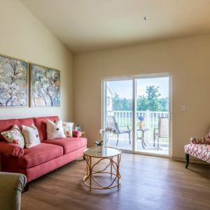 A cozy living room with a coral sofa, armchair, and artwork, featuring a sliding glass door leading to a balcony.