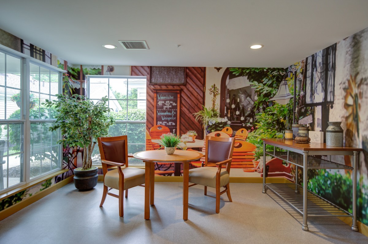 A cozy dining area with wooden furniture and lush indoor plants, complemented by a vibrant mural on the wall.