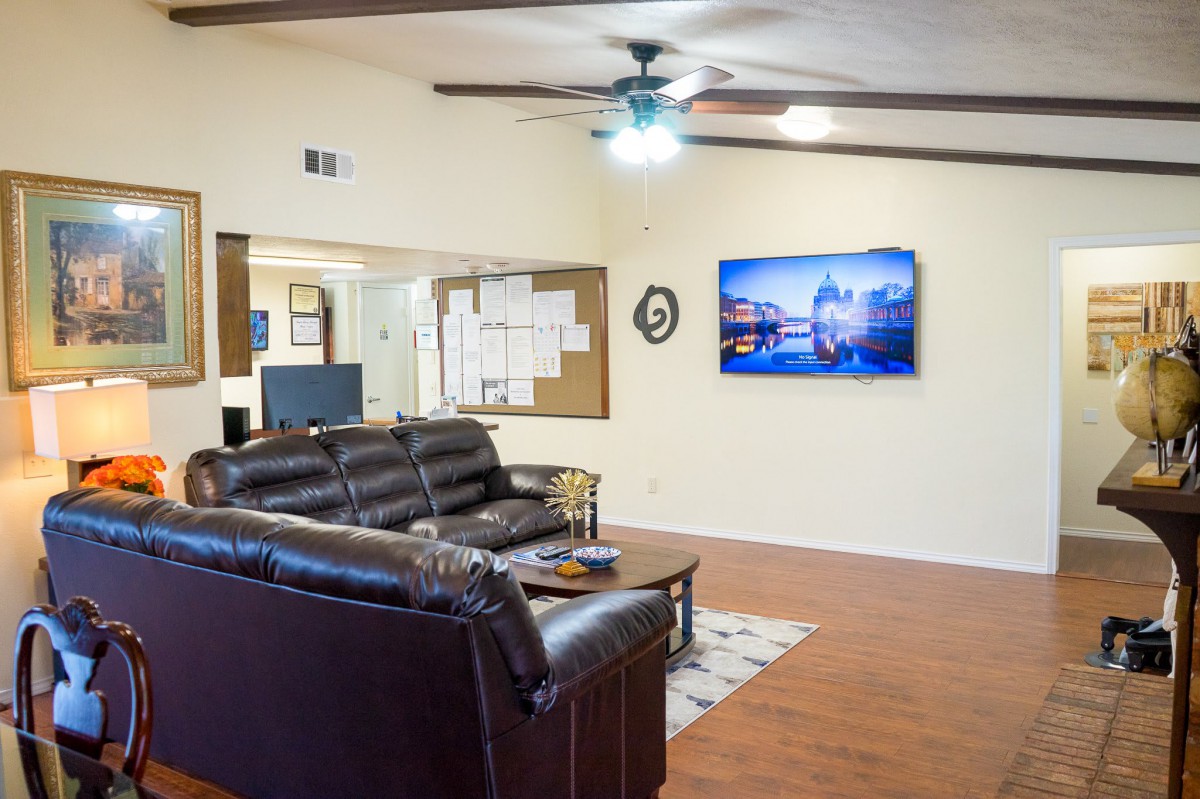 A cozy living room with a leather sofa, television, and ceiling fan.