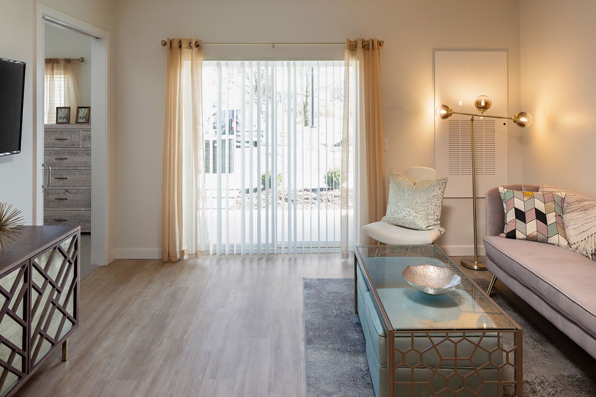 A bright and modern living room with minimalist decor, featuring a comfortable armchair, glass coffee table, and ample natural light streaming through sheer curtains.