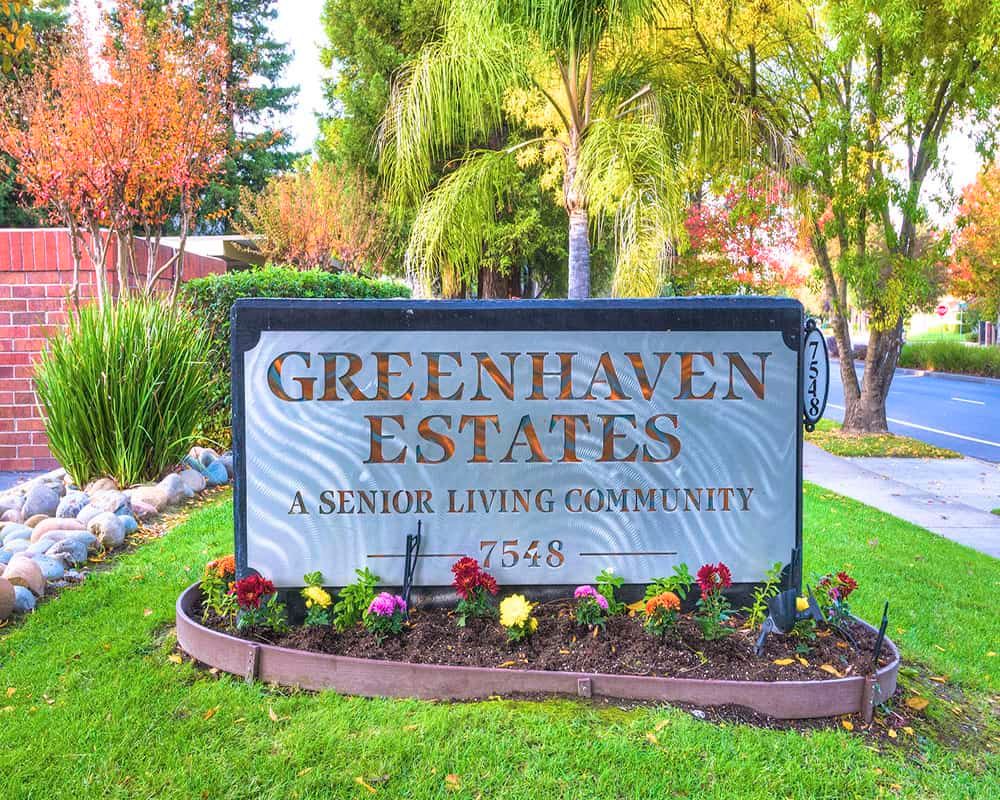 Entrance sign for Greenhaven Estates, a senior living community surrounded by landscaped gardens and trees.