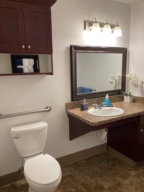 A clean and modern bathroom with a large mirror, sink, toilet, and wooden cabinets.