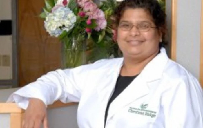 A person in a white coat smiling, with flowers in the background.