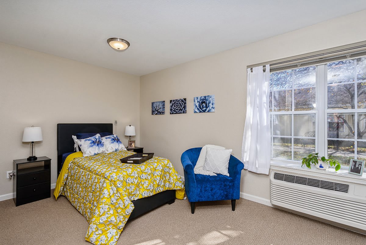 A cozy bedroom with a bed covered in a yellow patterned duvet, a bright blue chair, and decorative artwork on the wall.