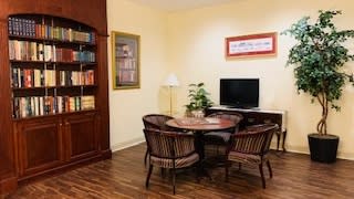 A cozy living room with a wooden bookshelf, table and chairs, TV, and a potted plant.