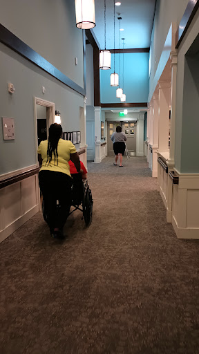 Two individuals walking in a brightly lit hallway, one pushing a stroller.