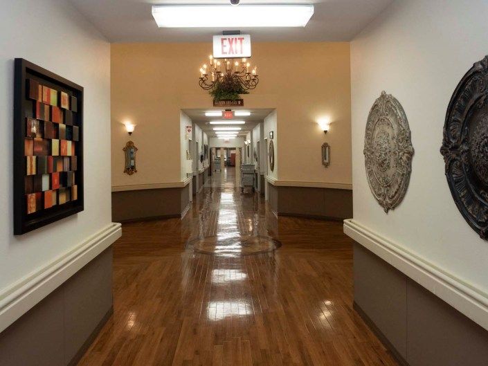 A well-lit hallway in a nursing home with wooden floors and decorative wall art.
