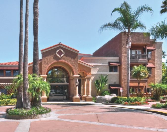 A sunny view of a hotel's entrance with palm trees and elegant architecture.