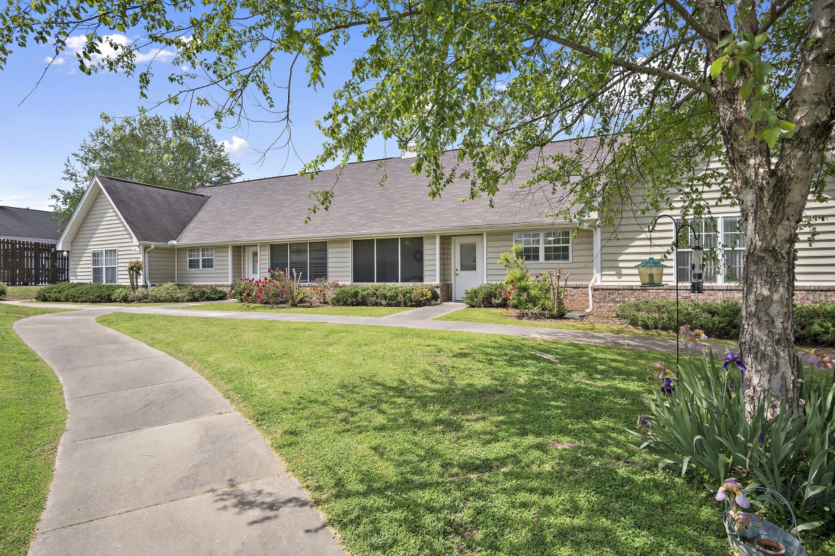 A suburban house with a well-maintained lawn and trees lining the sidewalk on a clear day.