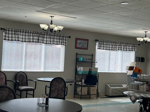 A cozy interior space featuring tables and chairs, with natural light filtering through checked curtains.