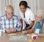 A caregiver assisting two seniors in playing a board game.
