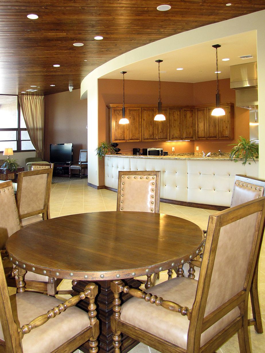 A spacious open-plan area featuring a dining room with a round wooden table and chairs, leading into a well-lit kitchen with pendant lights.