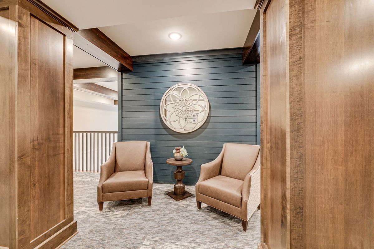 A cozy seating area featuring two chairs and a small table against a wood-paneled wall with a decorative clock.