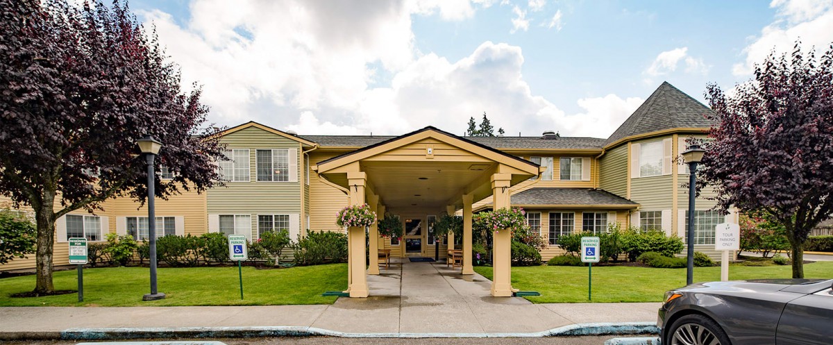 A residential building with a covered entrance and manicured landscaping under a partly cloudy sky.