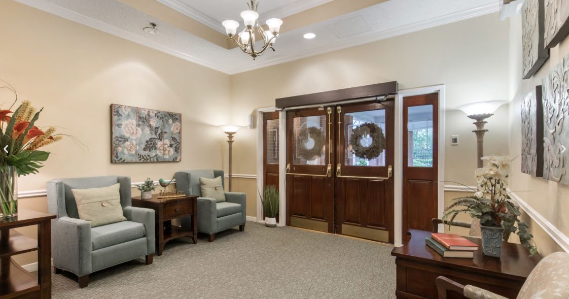 A cozy living room with comfortable chairs and elegant decor, featuring a chandelier and floral artwork.