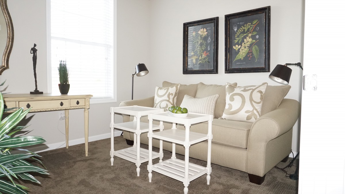 A cozy living room with a beige sofa, white coffee tables, and framed artwork on the wall.