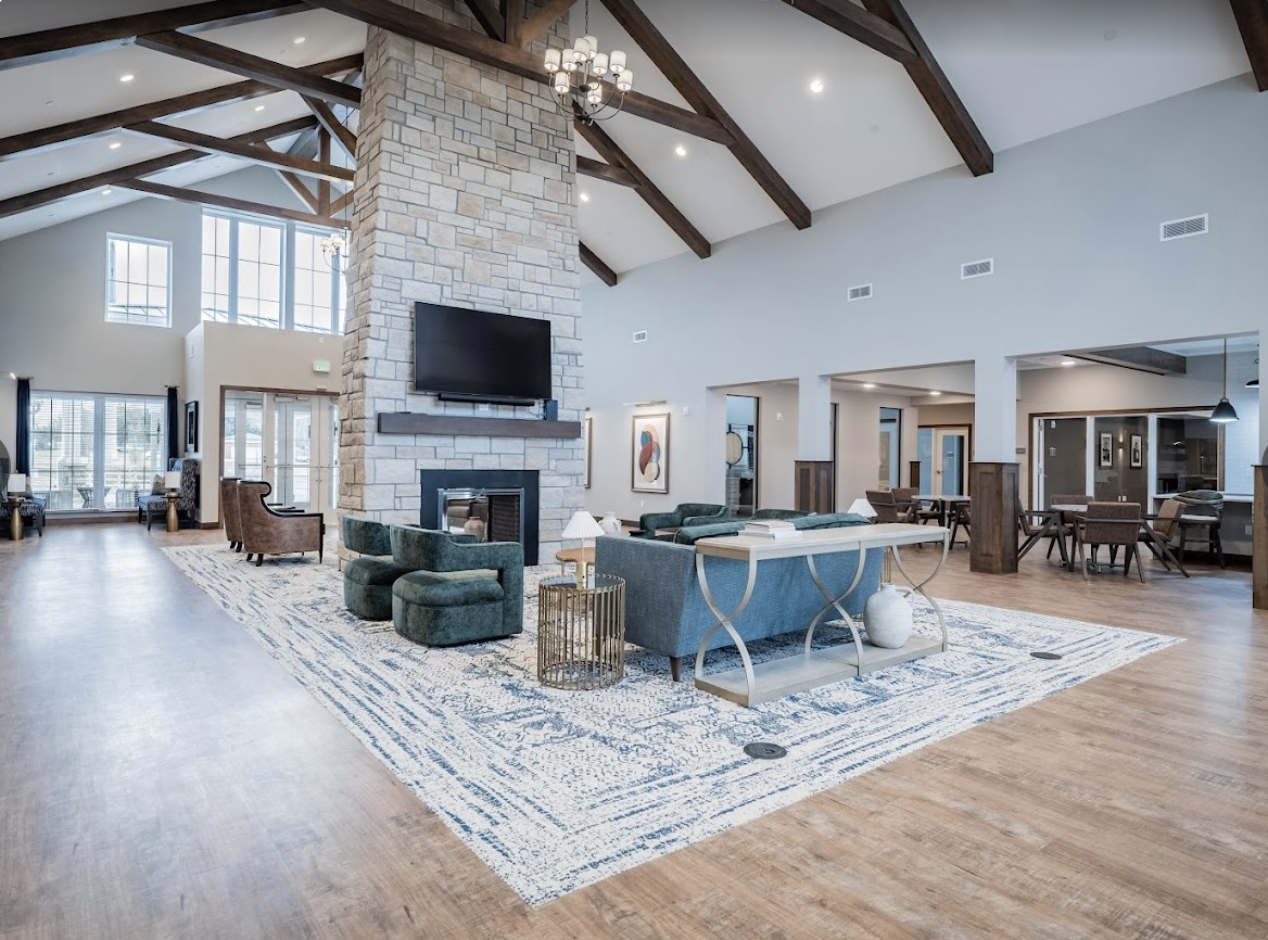 A spacious and modern living room with high ceilings, featuring a stone fireplace and elegant wooden beams.