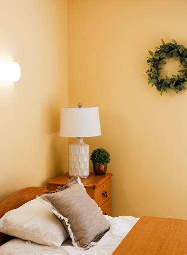 A cozy bedroom setup featuring a lamp and decorative elements against a warm yellow wall.