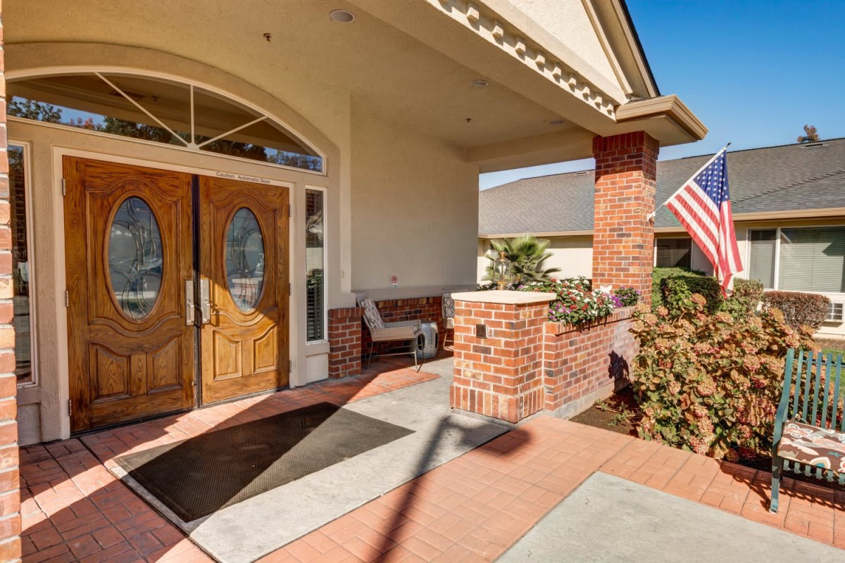 A brick porch entrance with double doors and decorative plants.