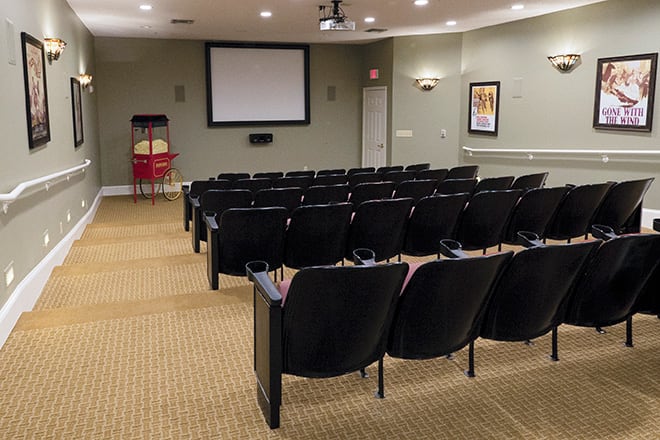 An empty theater room with rows of seats facing a screen.