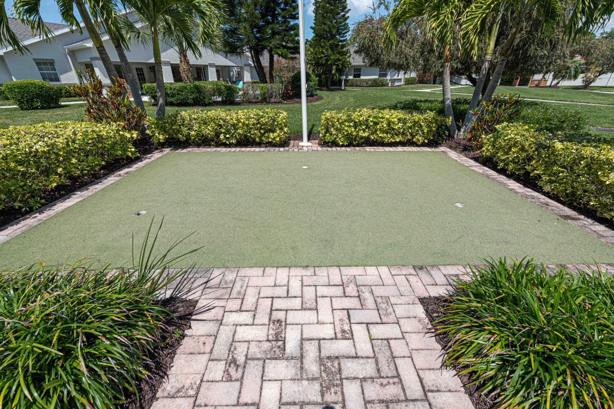 A small outdoor putting green surrounded by landscaping and a brick pathway.