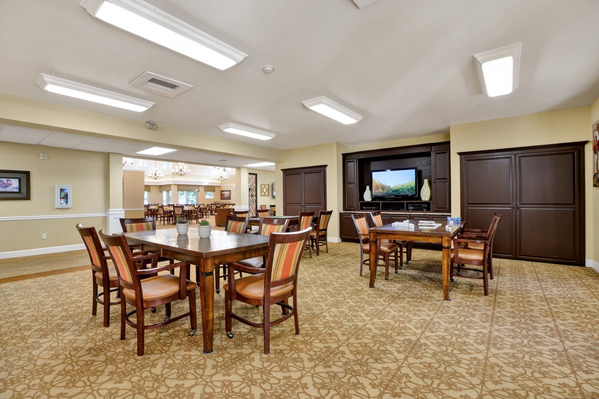 A spacious dining room with multiple tables and chairs, featuring a television and warm lighting.