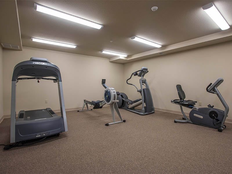 A gym room with various exercise equipment including a treadmill, elliptical, and stationary bike.