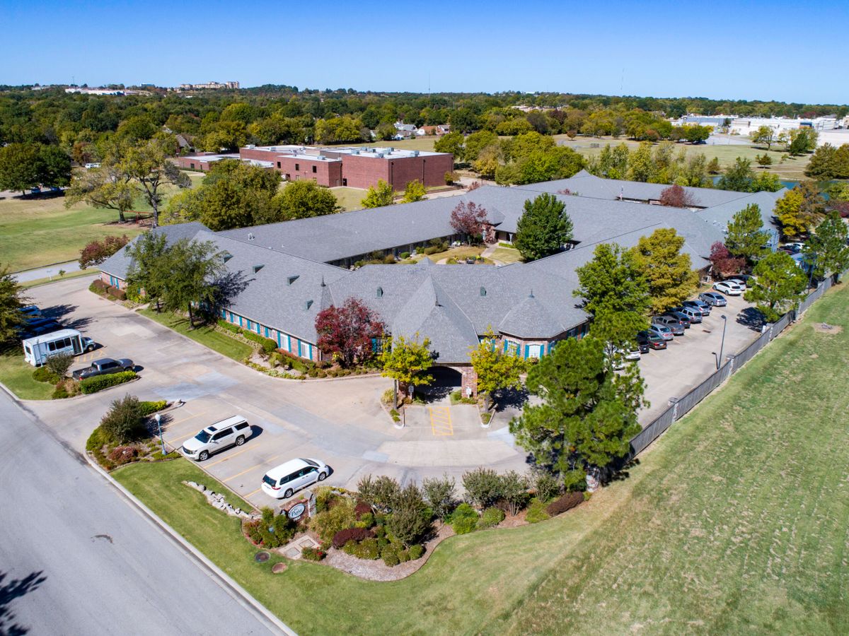 An aerial view of a large building surrounded by trees, with a parking lot and road nearby.