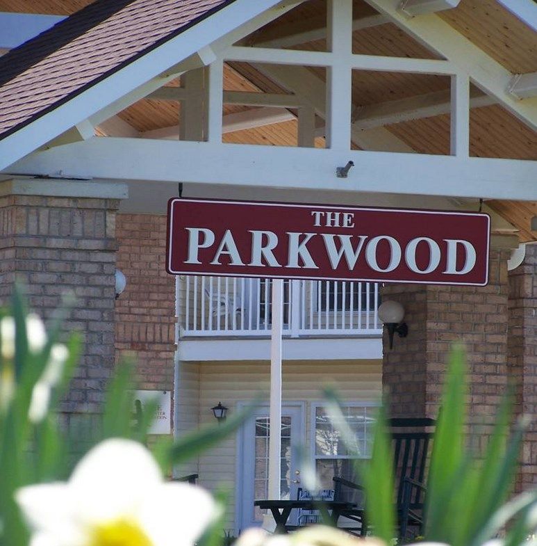 Entrance of a building with a sign reading 'The Parkwood', surrounded by flowering plants.