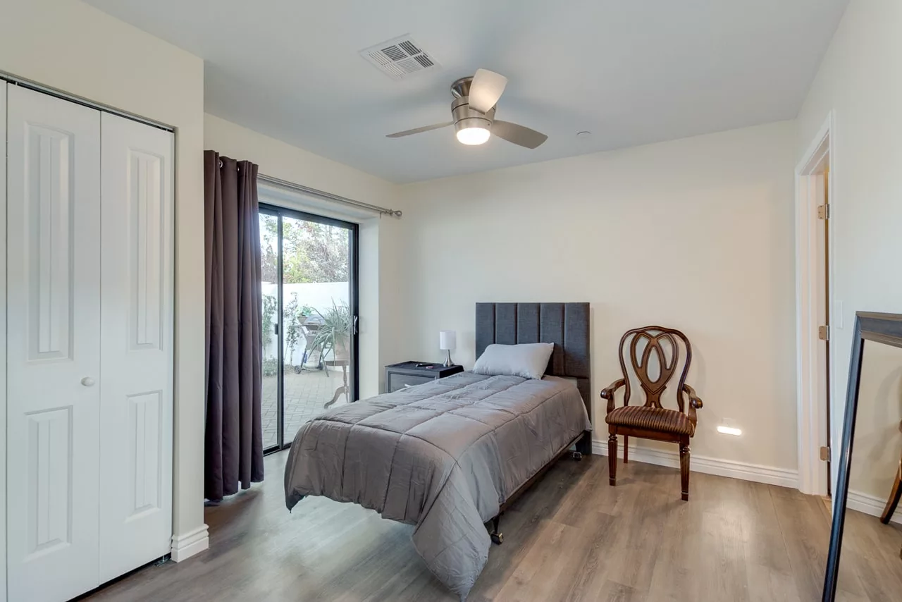 A simple bedroom with a single bed, gray bedding, and a wooden chair by the window.