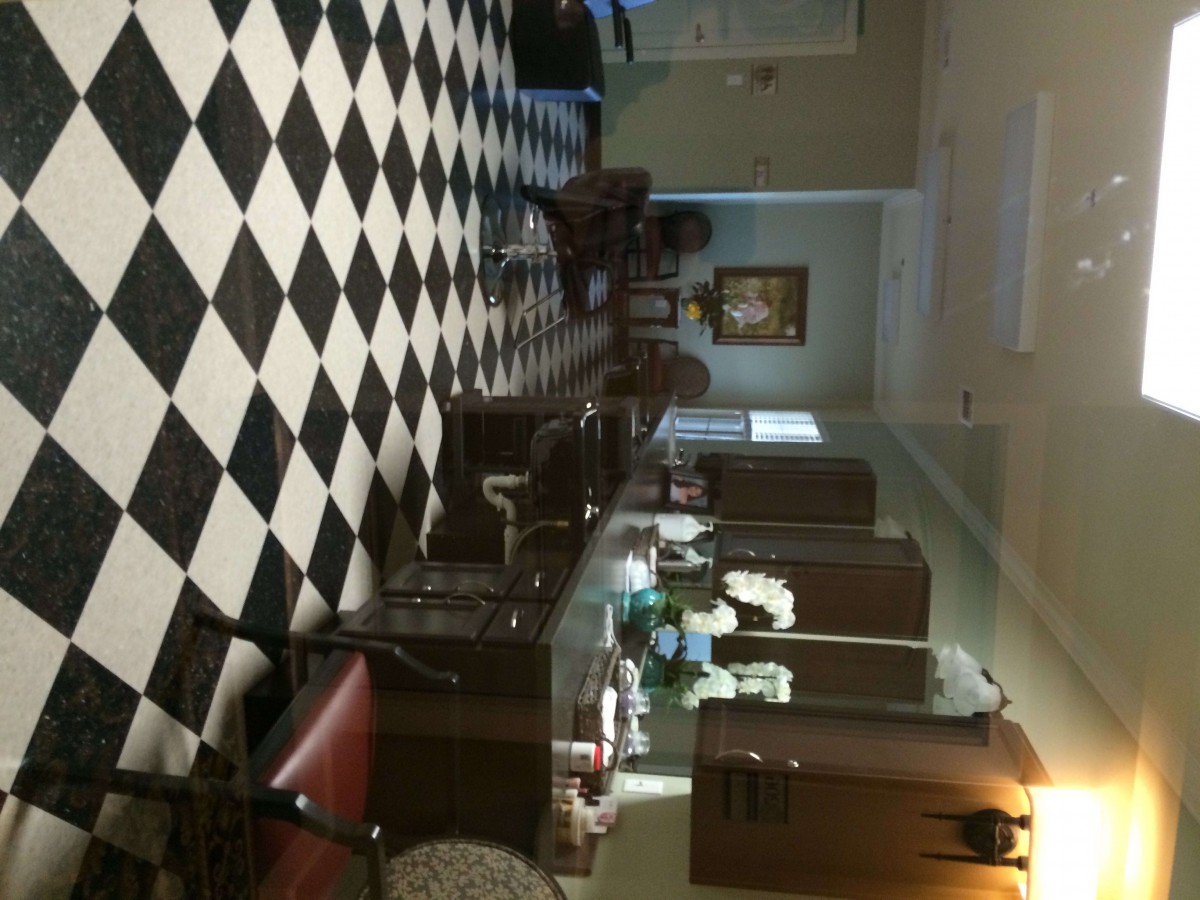 A kitchen interior with a black and white checkered floor, featuring tables, chairs, cabinets, and a painting on the wall.