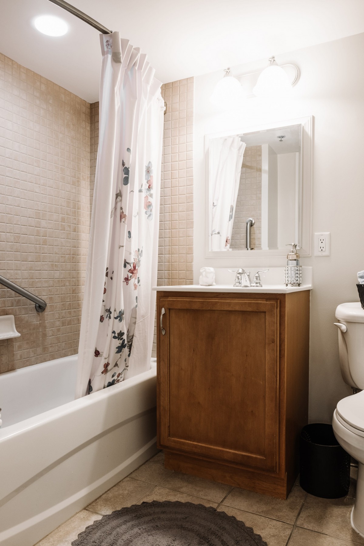 A cozy bathroom with a wooden vanity, a floral shower curtain, and bright lighting.