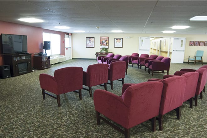 An empty lounge area with rows of red chairs facing a television.