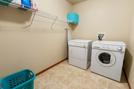 A tidy laundry room featuring a washing machine and dryer, with storage space and cleaning supplies organized on shelves.