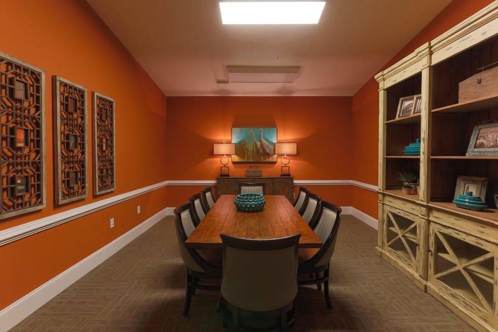 A warm and inviting conference room with orange walls, a long table with chairs, artwork on the wall, and shelves for storage.