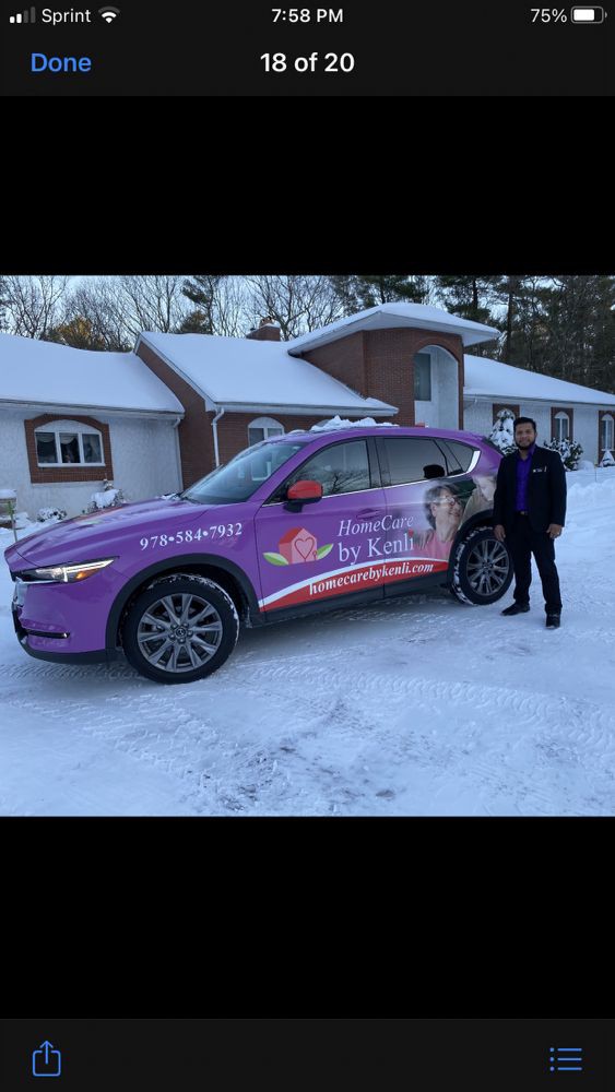 A person stands next to a purple wrapped car in a snowy driveway, with a house in the background.